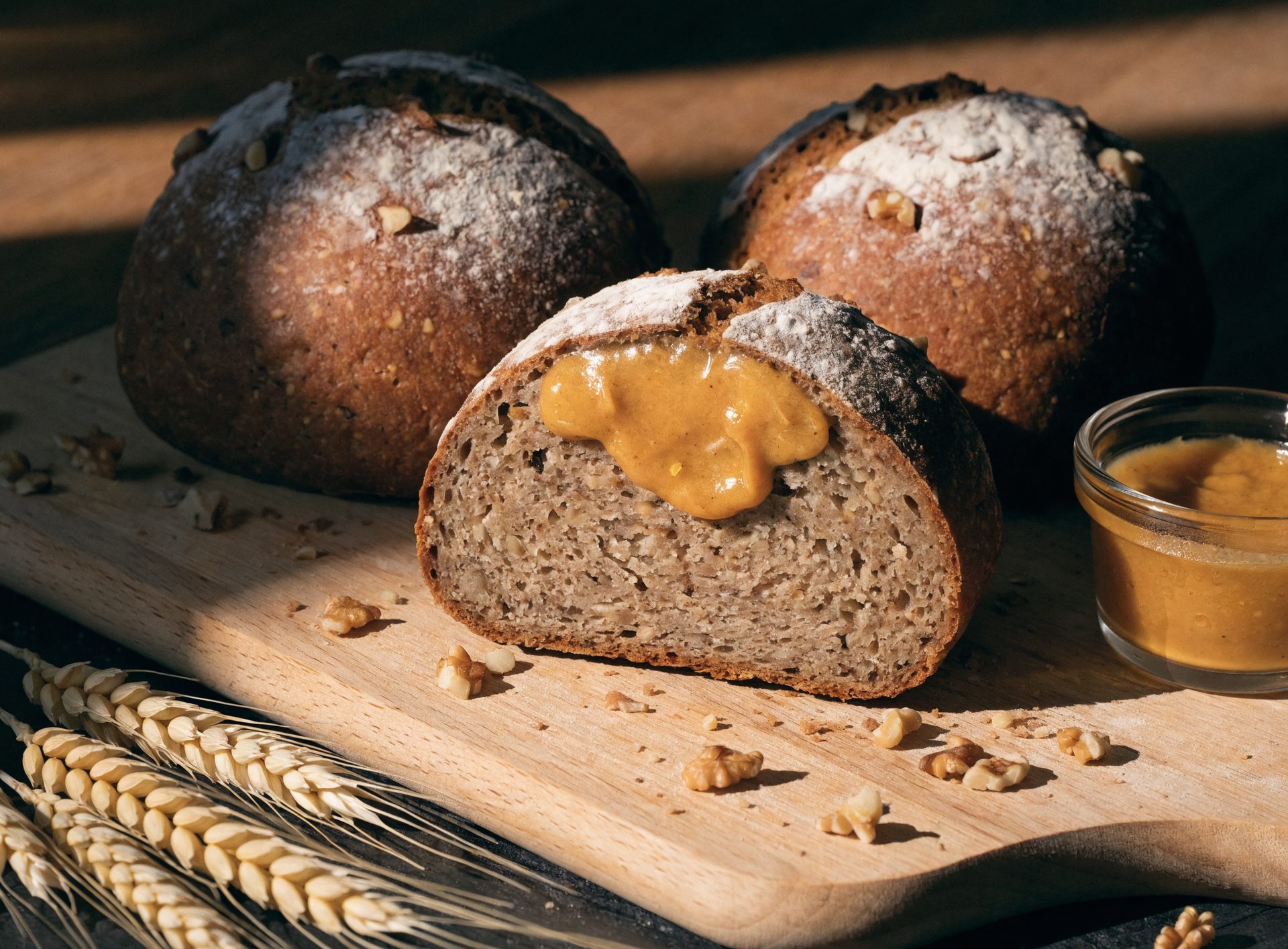 Drei rustikale Dinkel-Vollkorn-Brötchen, eines aufgeschnitten mit Honigsenf-Butter und Walnüssen